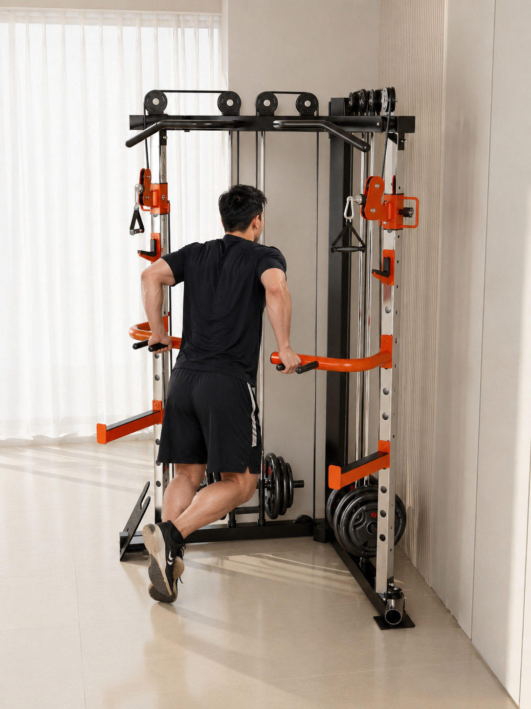 A man in a black t-shirt and shorts is using a cable pulley exercise machine with orange accents in a bright, modern home gym setting.