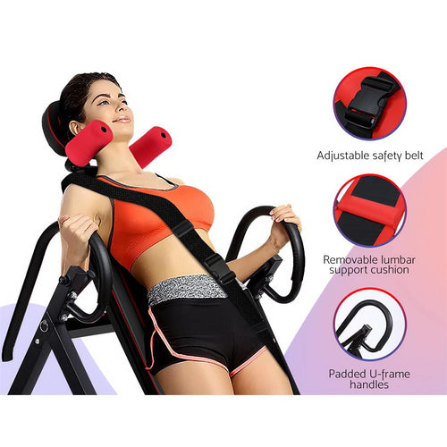 Woman using Inversion Table with adjustable safety belt, lumbar support cushion, and padded handles for back stretching.