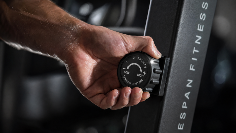 A close-up of a person's hand adjusting a tension control dial on a black gym machine labeled 'ESPAN FITNESS'.
