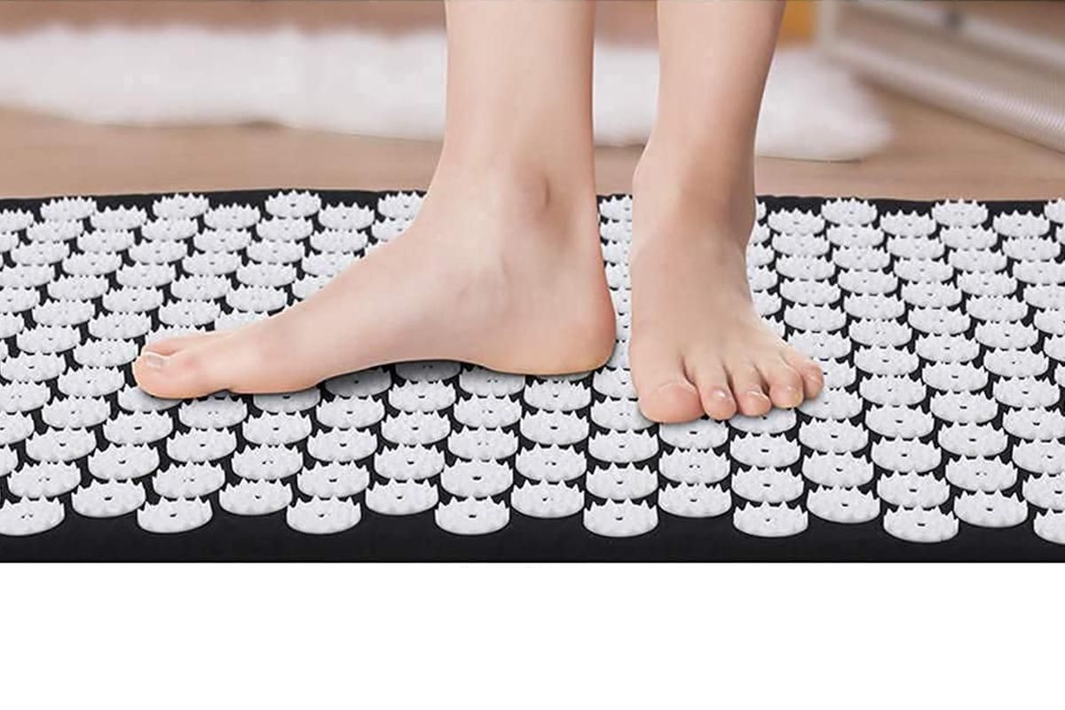 Person standing on an acupressure mat and pillow set with visible pressure points for relaxation.