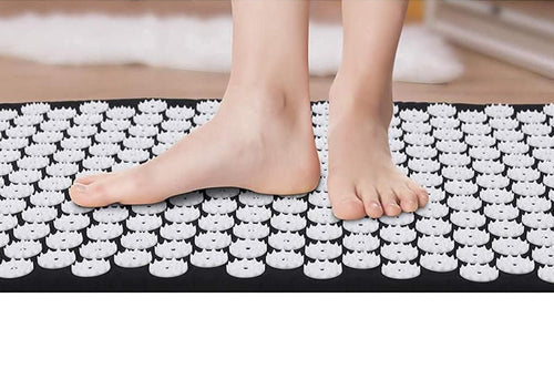 Person standing on an acupressure mat and pillow set with visible pressure points for relaxation.