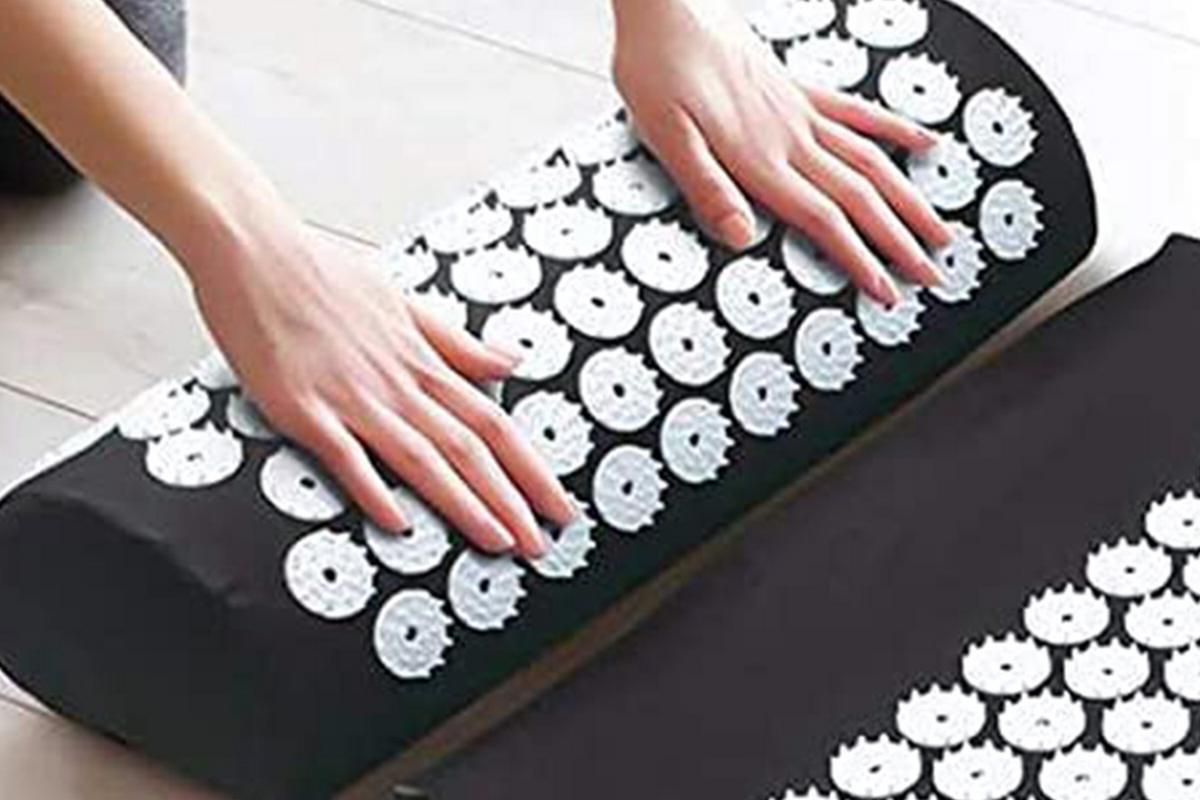 Person using an acupressure mat and pillow set to relieve tension with acupressure points.