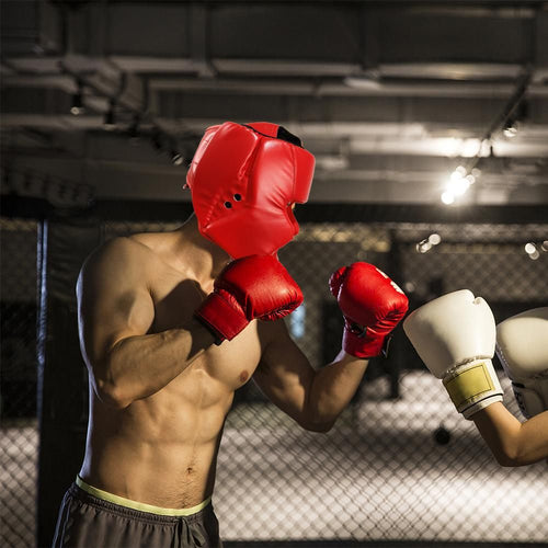 Adult athlete wearing red boxing head gear and gloves during training in a training facility.
