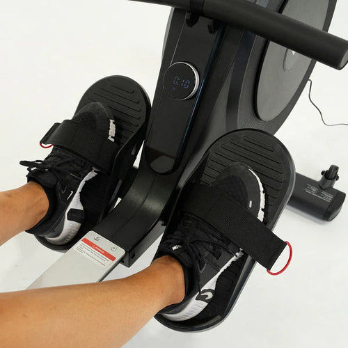 Close-up of feet on rowing machine pedals, showcasing secure foot straps and digital display.